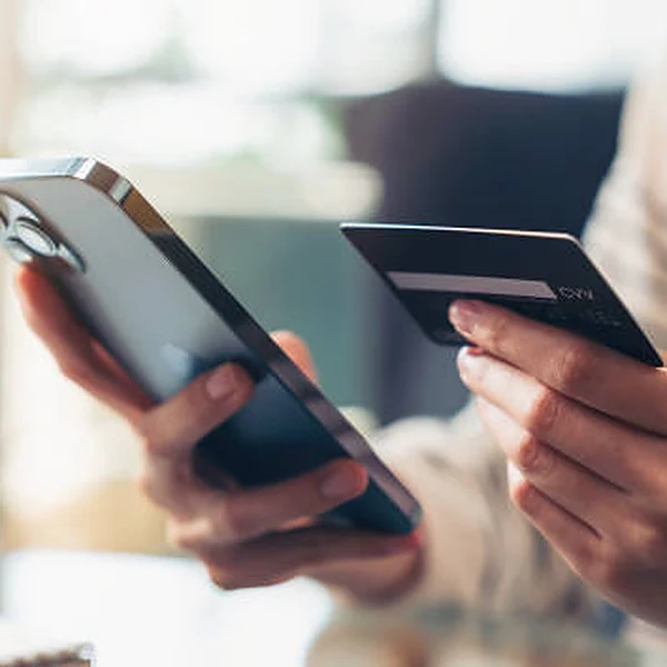 A customer holding a phone in one hand and a credit card in the other, paying online